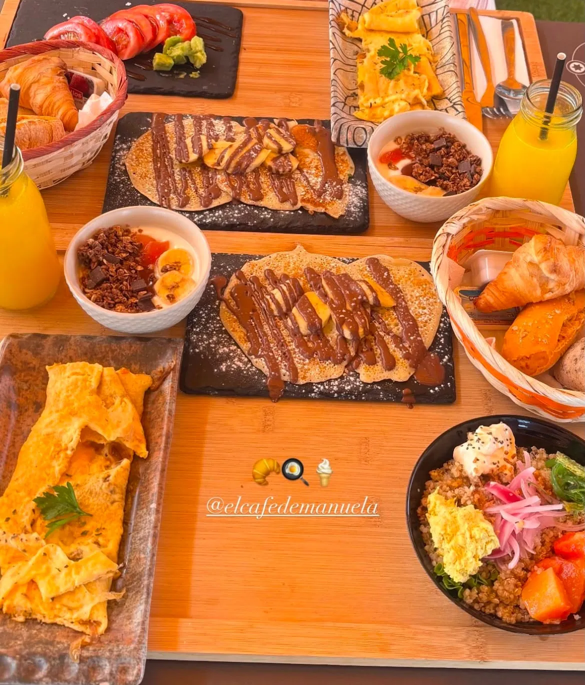 Brunch table with two banana and chocolate pancakes, an omelette, granola yoghurts and a quinoa bowl