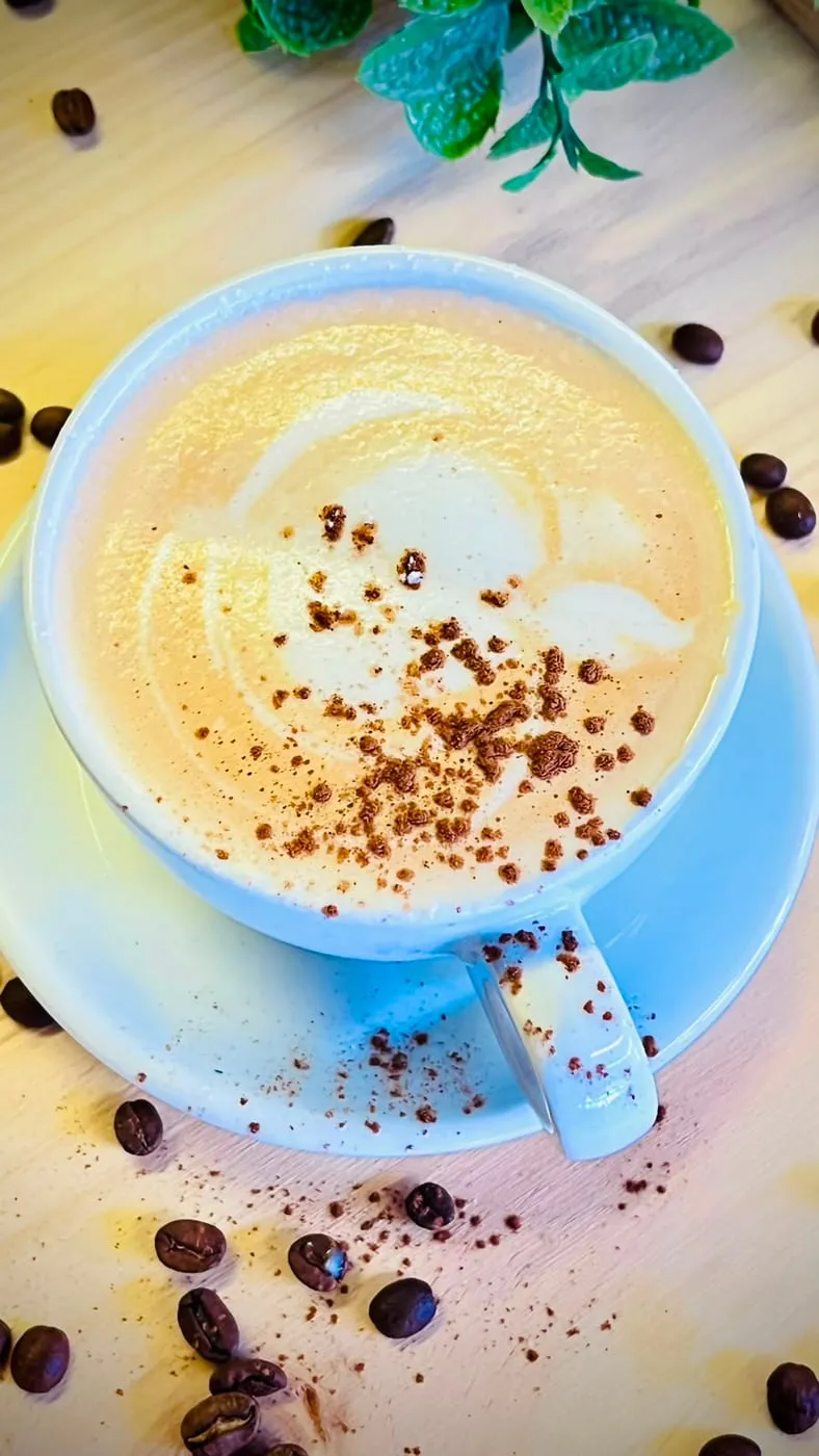 Cappuccino dusted with cocoa, among coffee beans